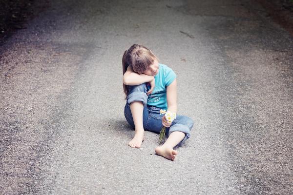 Kleines Mädchen sitzt auf einer Straße mit Blumen in der Hand als Sinnbild für unser inneres Kind
