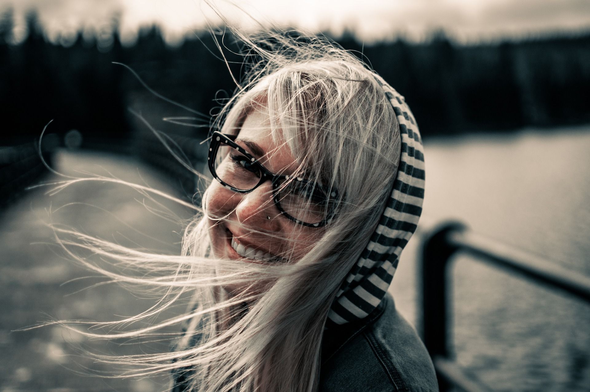 Junge frau mit Brille und Kapuze, wehenden Haaren und einem Lächeln zeigt, wie selbstbewusst mit Kritik umgehen kann