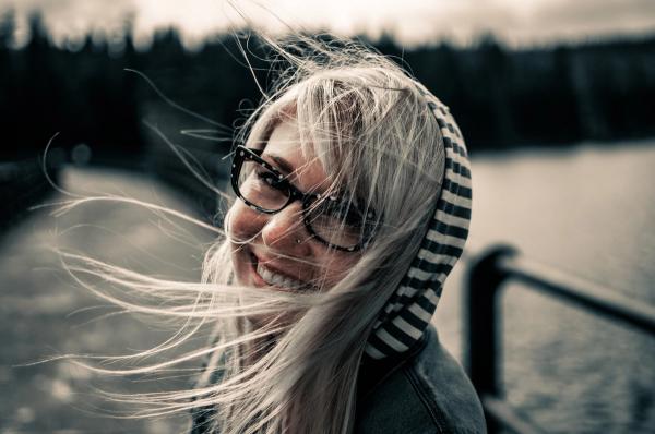 Junge frau mit Brille und Kapuze, wehenden Haaren und einem Lächeln zeigt, wie selbstbewusst mit Kritik umgehen kann