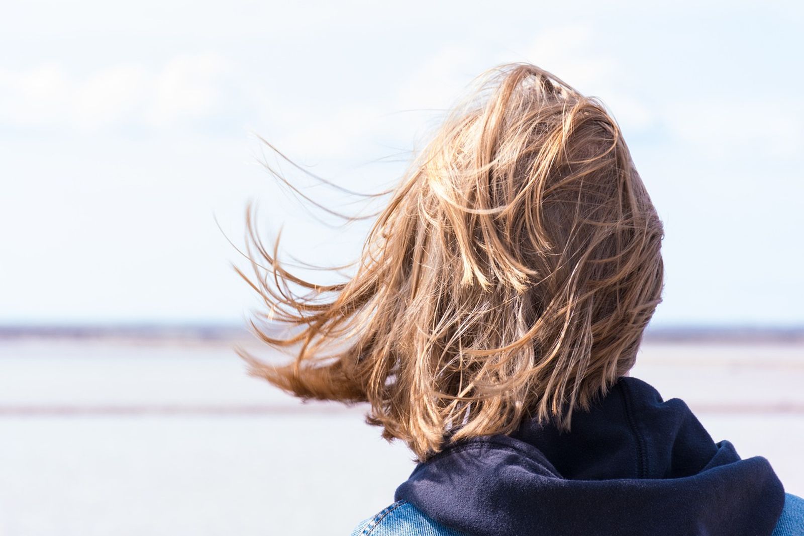 Frau im Wind blickt mutig auf Meer als Sinnbild für den Mut zur Veränderung