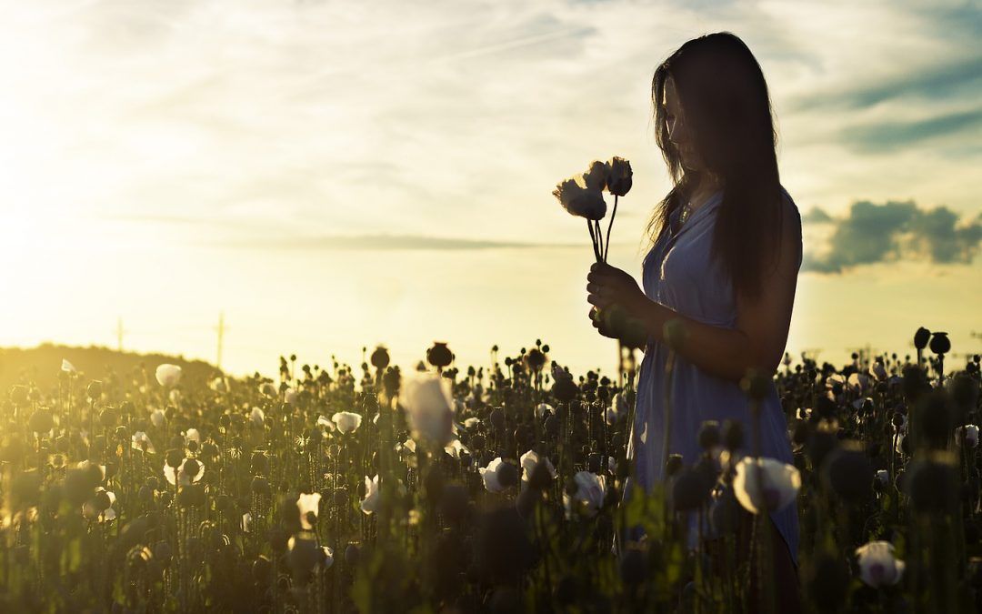 Frau mit zwei Blumen in der Hand im dämmrigen Blumenfeld als Sinnbild, wie Dankbarkeit unser Leben zum Erblühen bringt