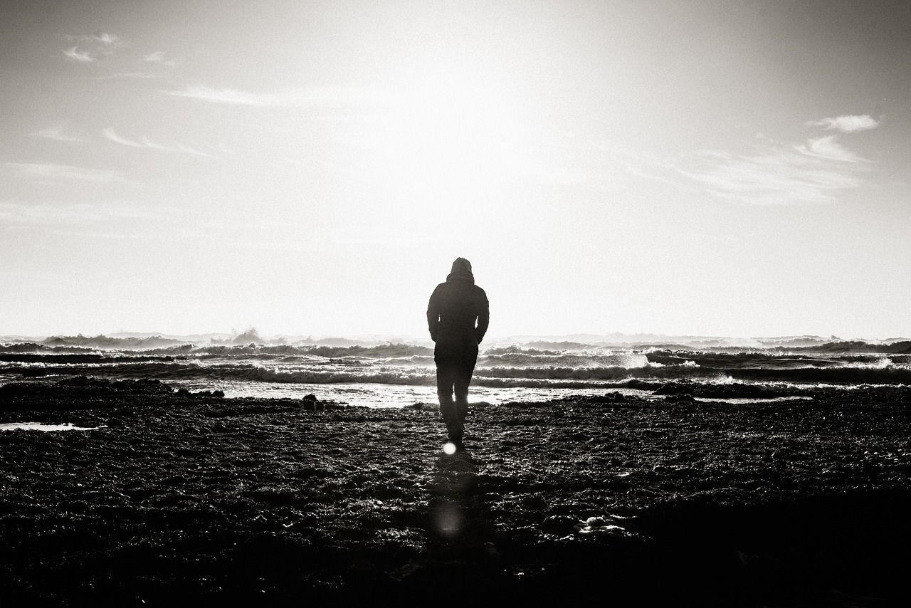 Mann am Strand in schwarz-weiß, die Wellen vor ihm als Sinnbild für Gedanken, mit denen wir uns selbst blockieren
