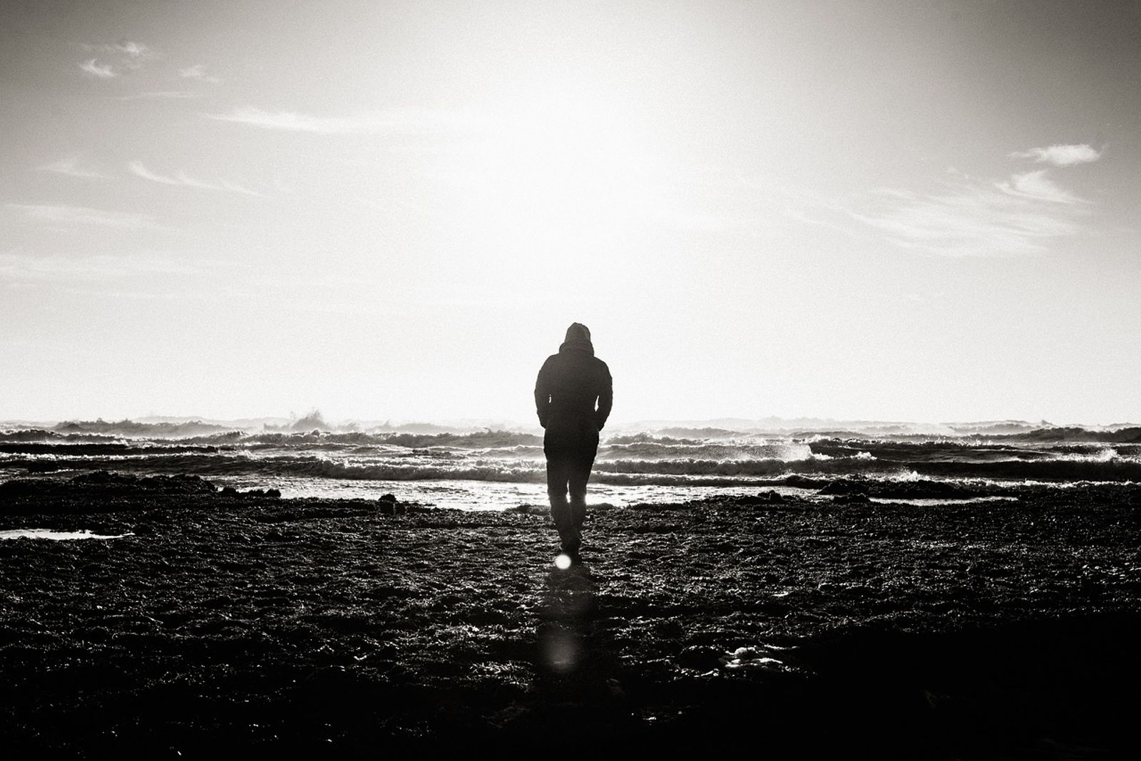 Mann am Strand in schwarz-weiß, die Wellen vor ihm als Sinnbild für Gedanken, mit denen wir uns selbst blockieren