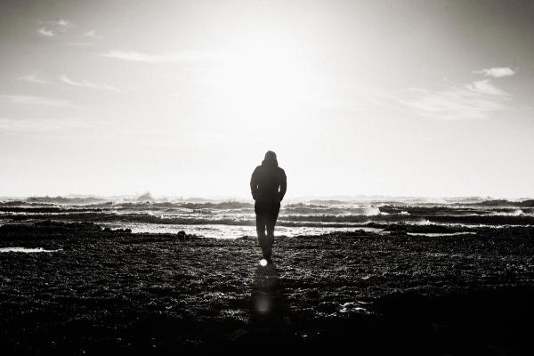 Mann am Strand in schwarz-weiß, die Wellen vor ihm als Sinnbild für Gedanken, mit denen wir uns selbst blockieren