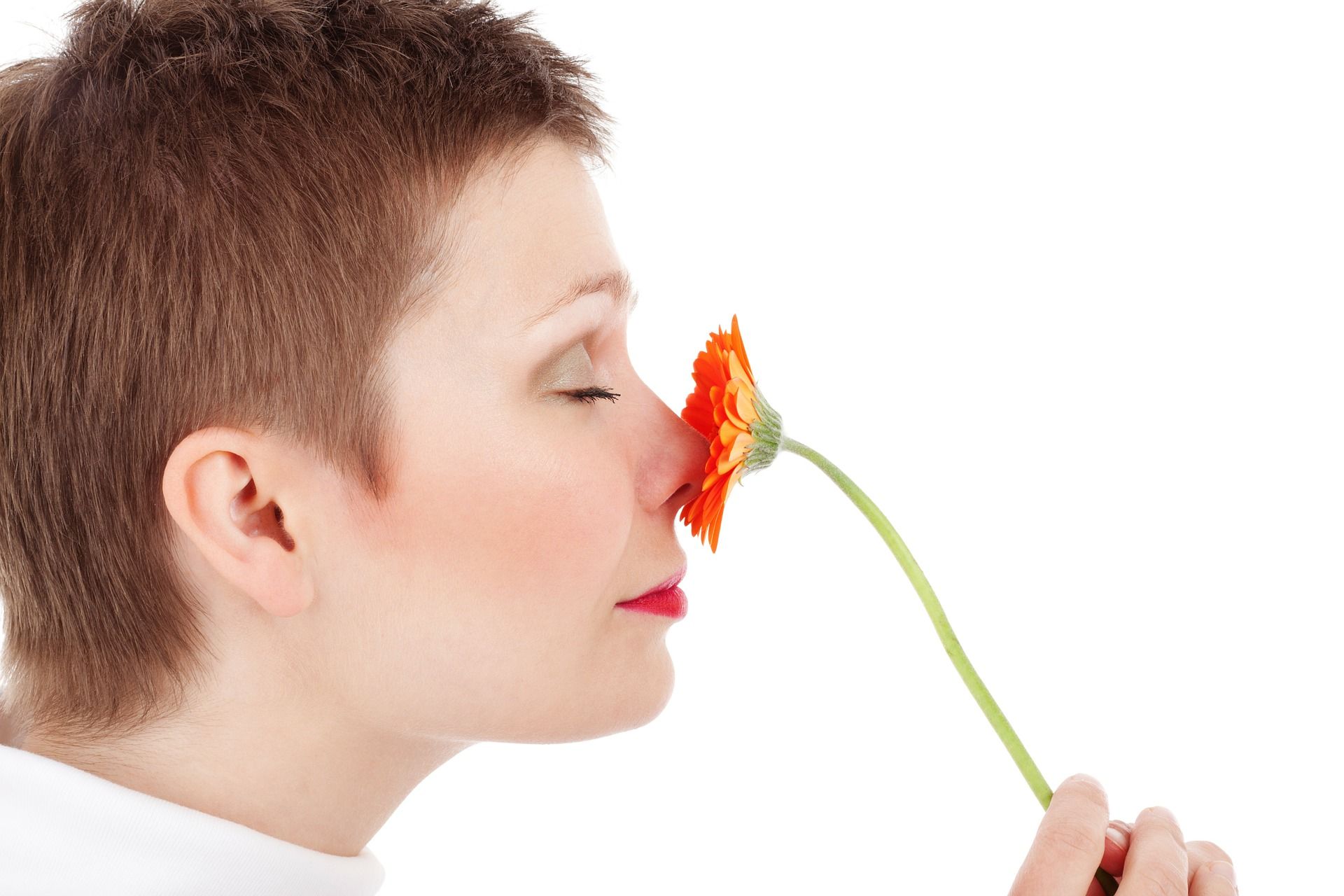 Frau riecht mit geschlossenen Augen an einer orangen Gerbera und überlegt, wie sie dieses Glück verschenken kann