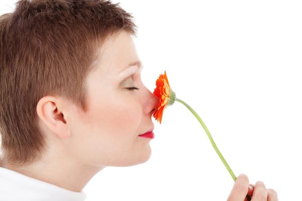 Frau riecht mit geschlossenen Augen an einer orangen Gerbera und überlegt, wie sie dieses Glück verschenken kann