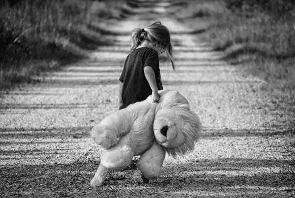 Kleines Mädchen auf einem sandigen Weg hat einen großen Kuscheltier-Löwen in der Hand