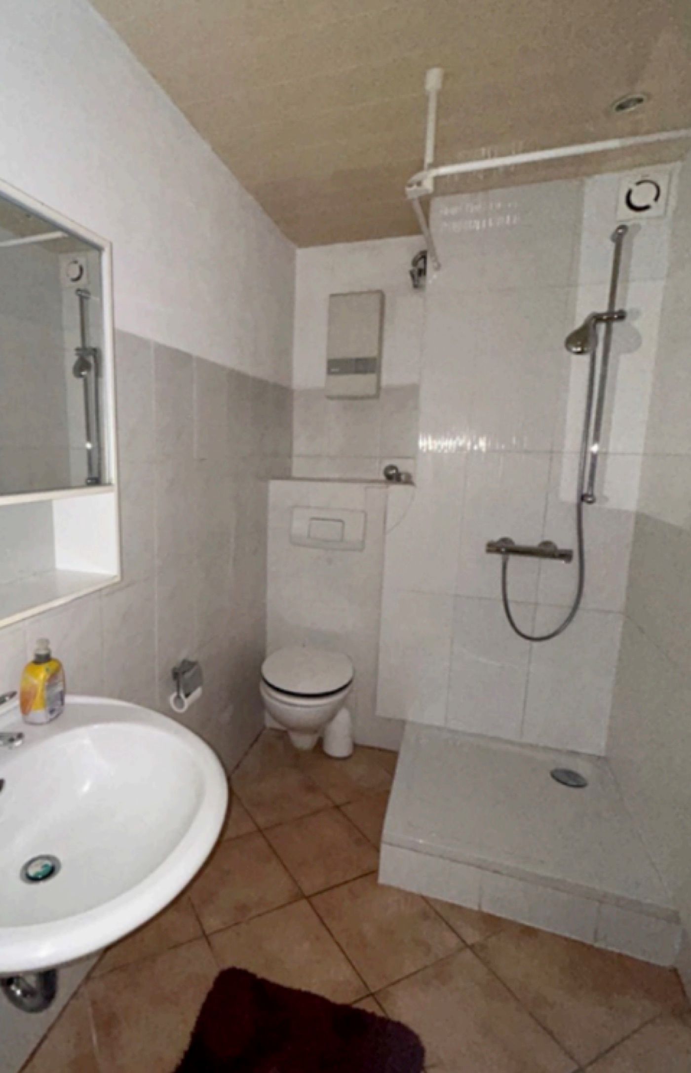 Das Badezimmer vor der Sanierung: beige Bodenfliesen, Waschbecken mit Standfuß und Dusche mit Vorhangstange.