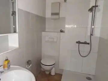 Das Badezimmer vor der Sanierung: beige Bodenfliesen, Waschbecken mit Standfuß und Dusche mit Vorhangstange.