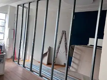 Das Ständerwerk der neuen Trennwand steht, dahinter der noch offene Raum mit Leiter und Gipsplatten.