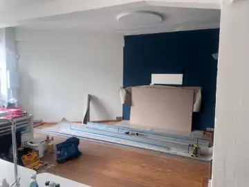 Während des Umbaus: Trockenbauprofile liegen auf den alten Dielen bereit, die dunkelblaue Wand ist abgedeckt.