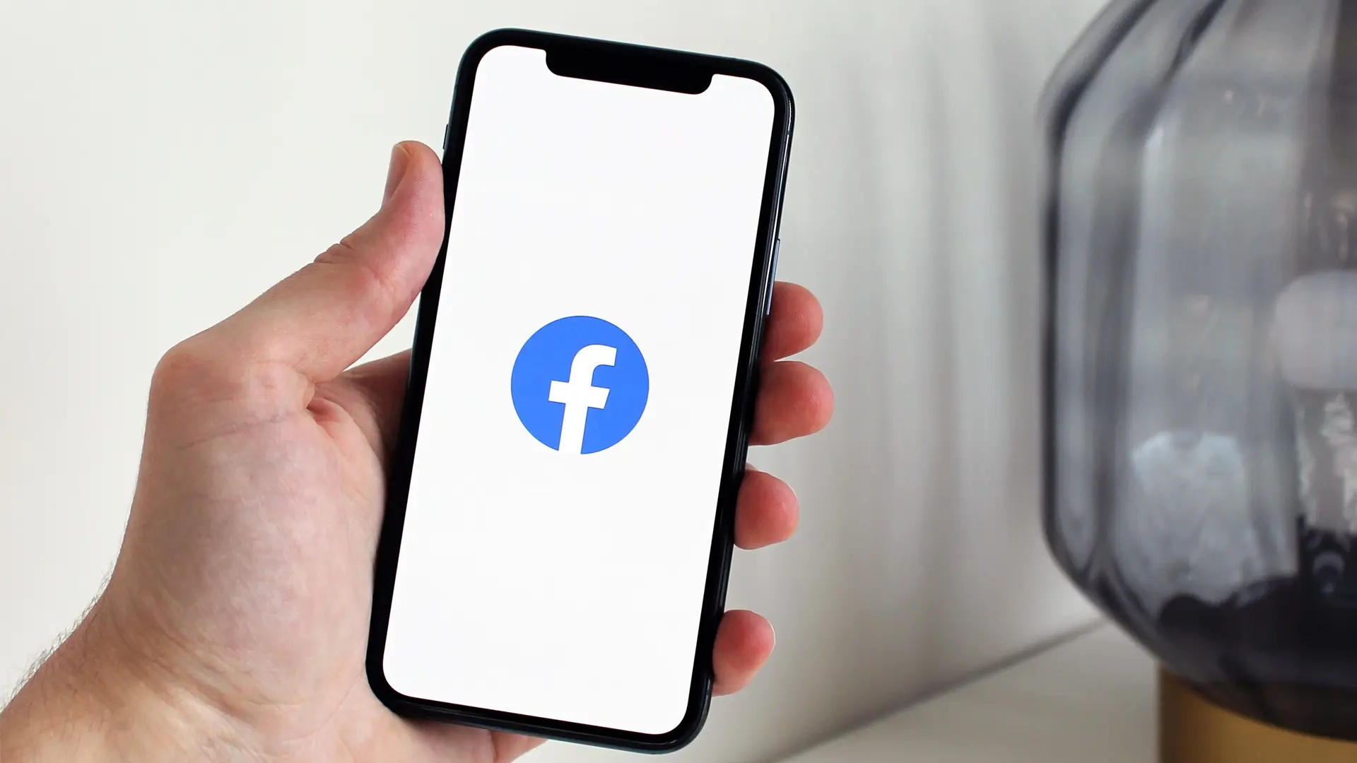 Hand håller upp en Iphone som visar Facebooks logotyp.