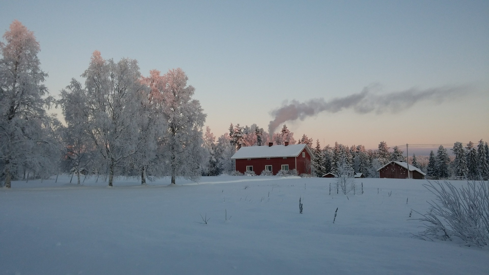 Vinterlandskap, ett hus täckt av snö med skorstensrök.
