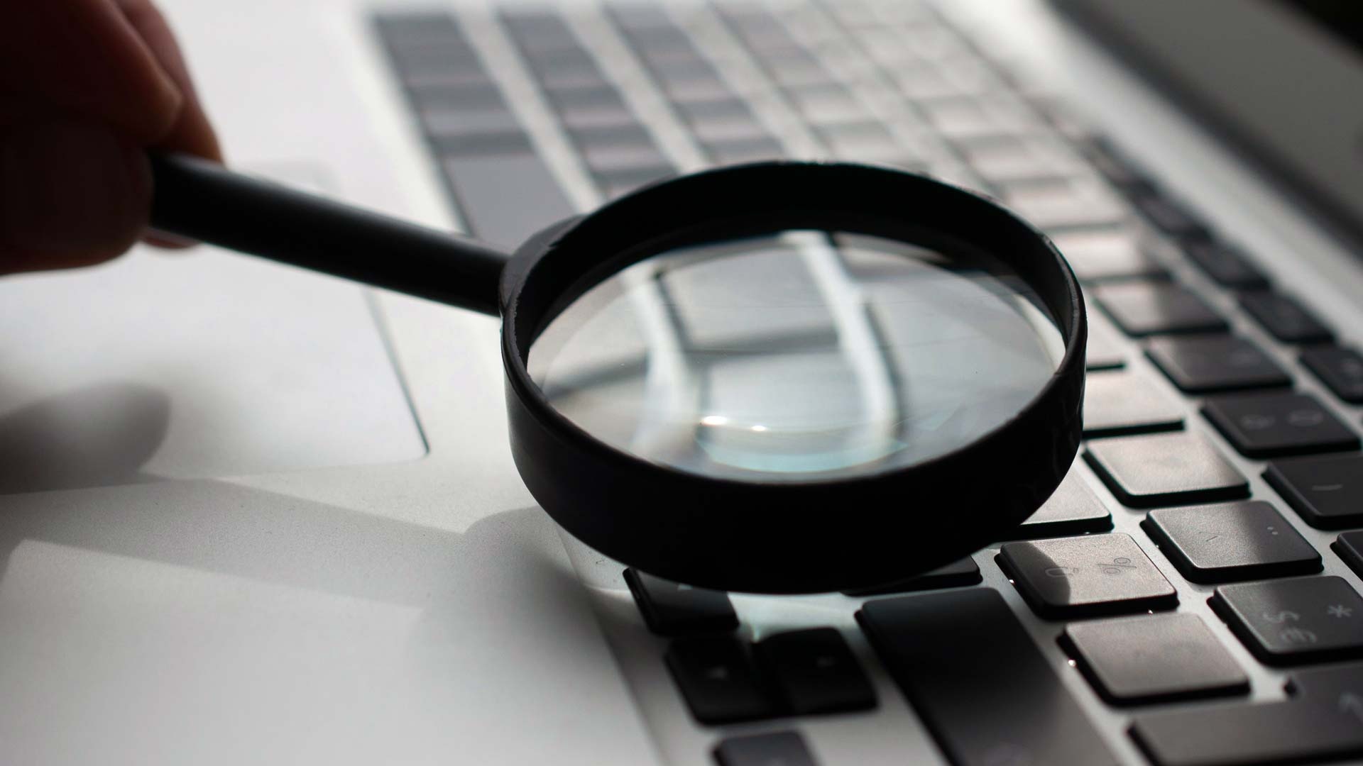 En person håller ett förstoringsglas ovanpå en bärbar dators tangentbord.