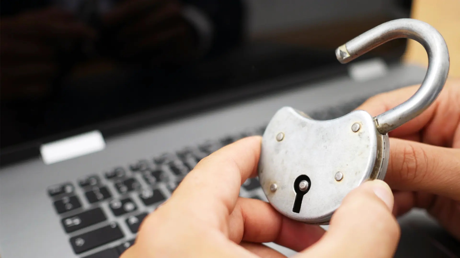 Person håller ett upplåst hänglås intill en bärbar dator.