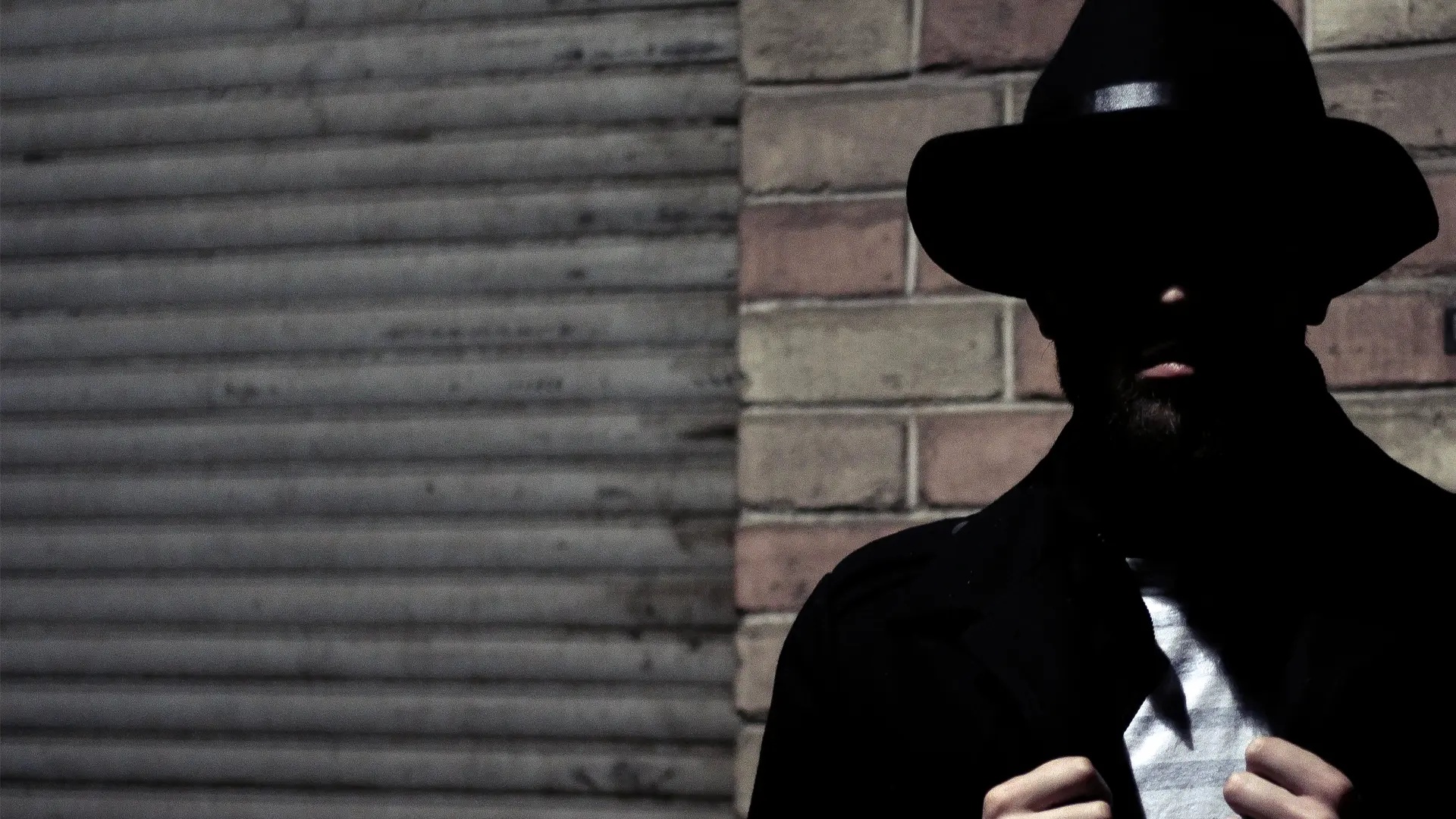 Stereotyp spion i fedorahatt står intill en tegelvägg.