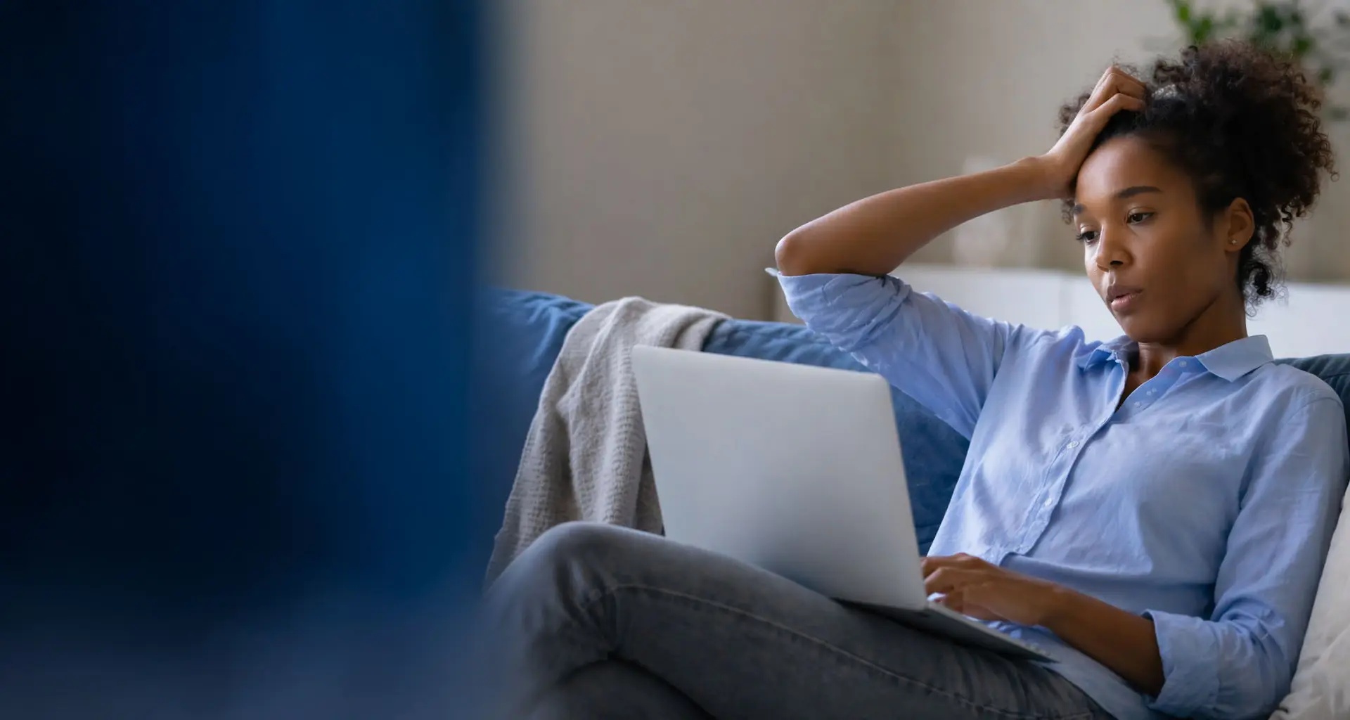 Ung kvinna sitter i en soffa med sin bärbara dator och ser orolig ut.