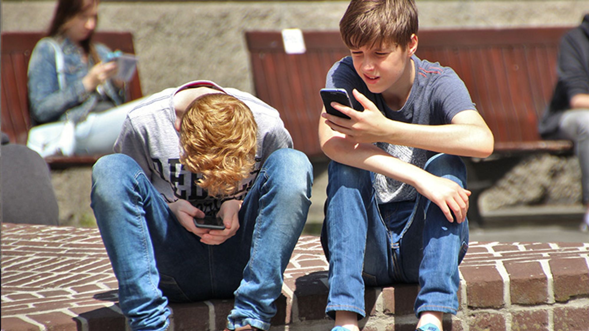 Två pojkar som sitter utomhus och tittar på sina mobiltelefoner