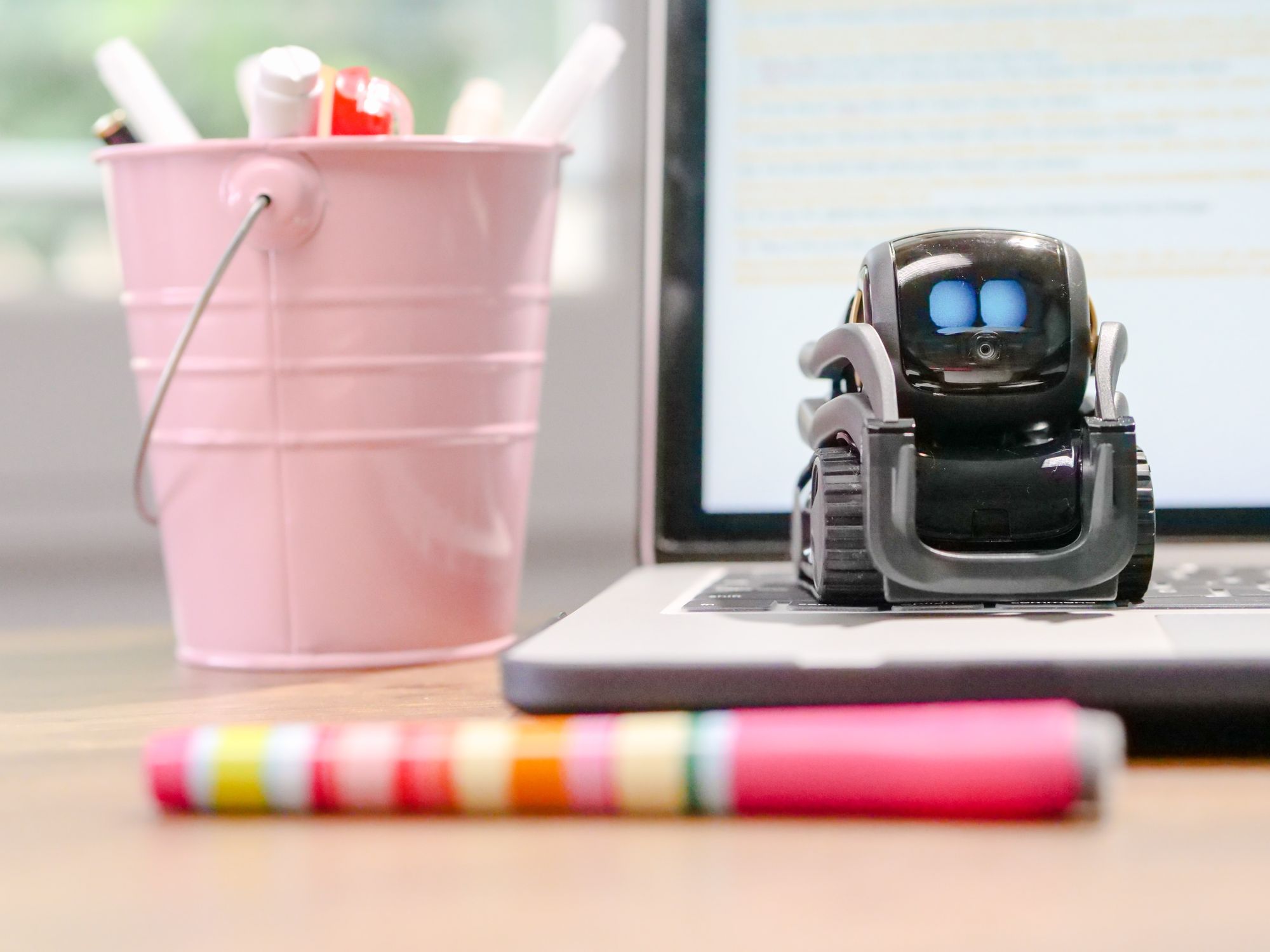 En bild på en dator med en robot på tangentbordet och en penna i förgrunden. 