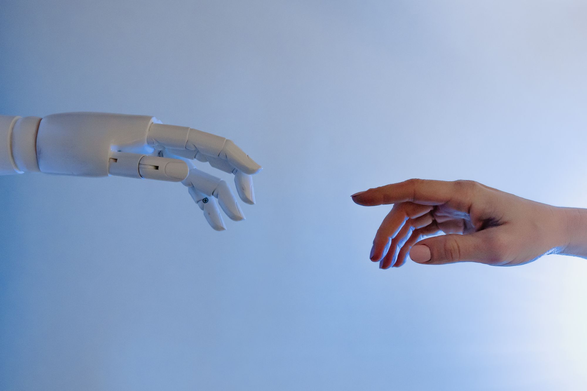 Bild på en robothand och en mänsklig hand som möts, med en ljusblå bakgrund.