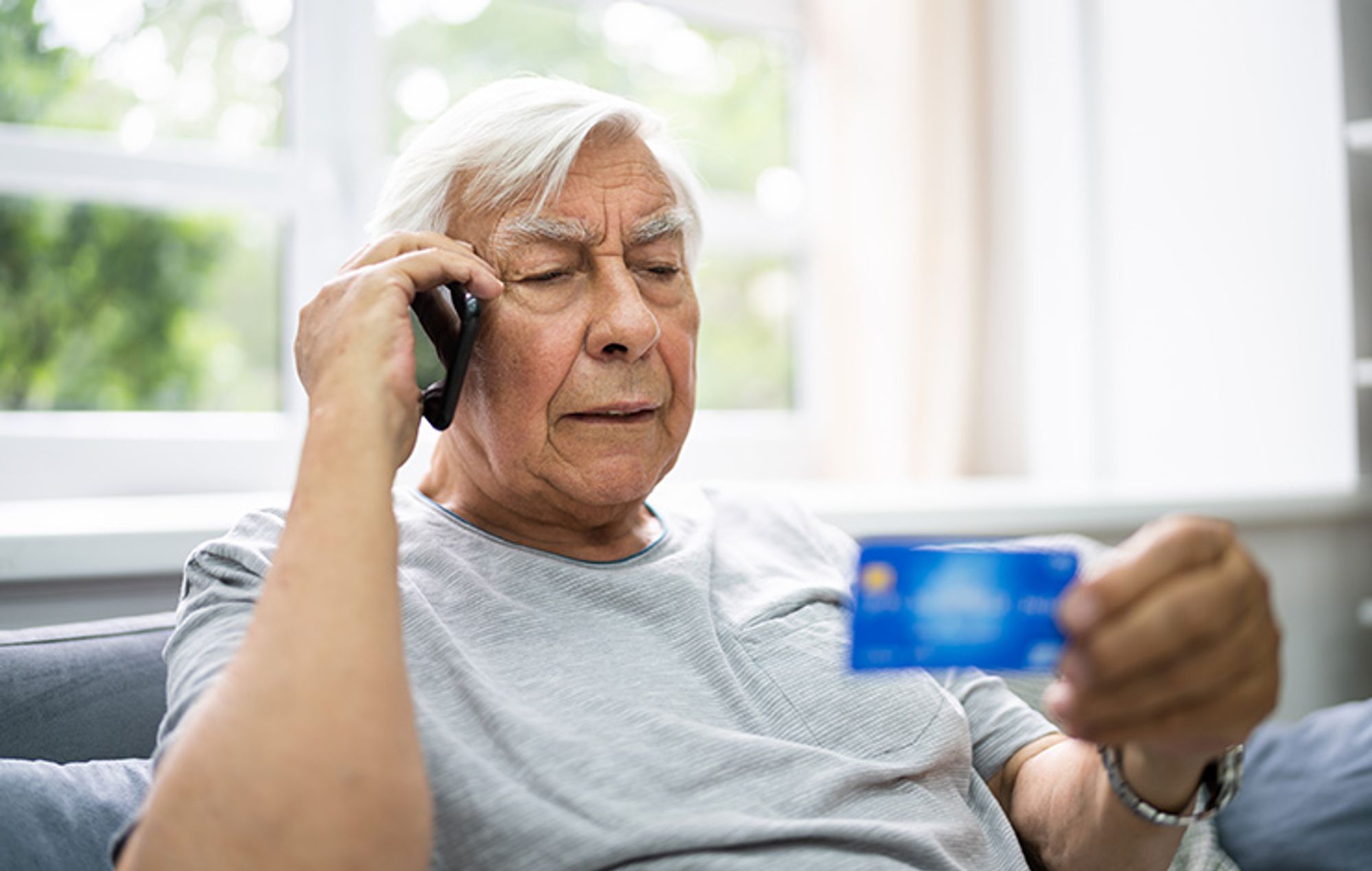 Äldre man pratar i mobiltelefon samtidigt som han tittar på ett betalkort 