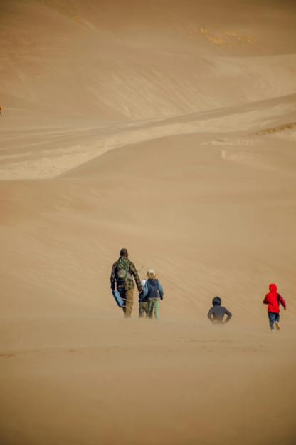 a group of people are walking down a sand dune .