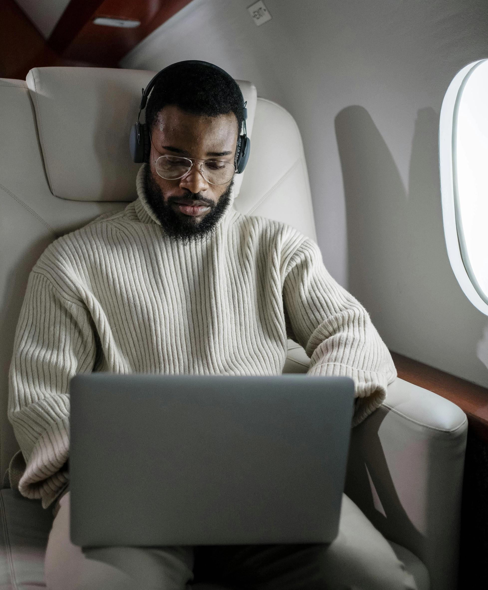 a man wearing headphones is using a laptop on an airplane .