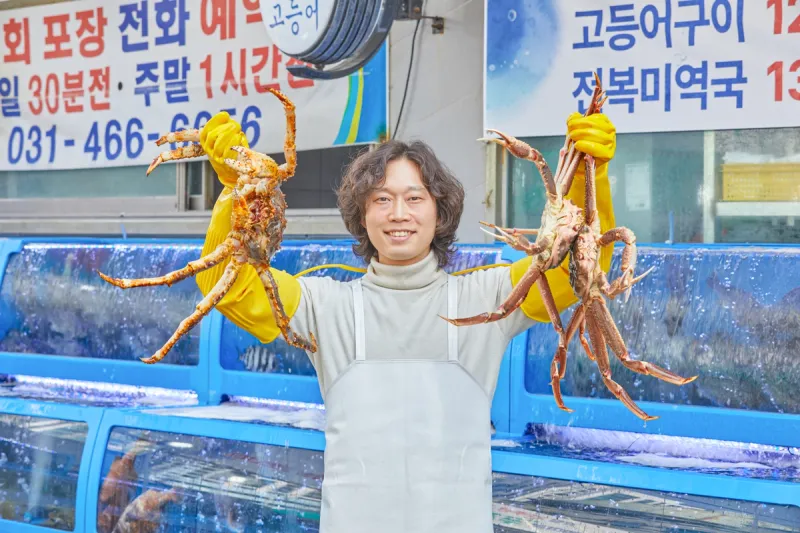 여자수산 안양본점 대표가 활게를 양손에 든 모습, 수족관 앞
