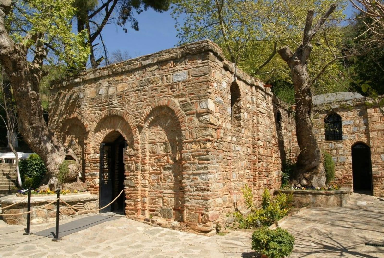 An ancient stone and brick building surrounded by green trees in sunlight.