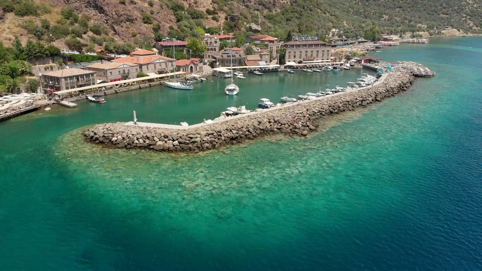 Aerial view of a picturesque harbor town with clear turquoise water and a stone breakwater.