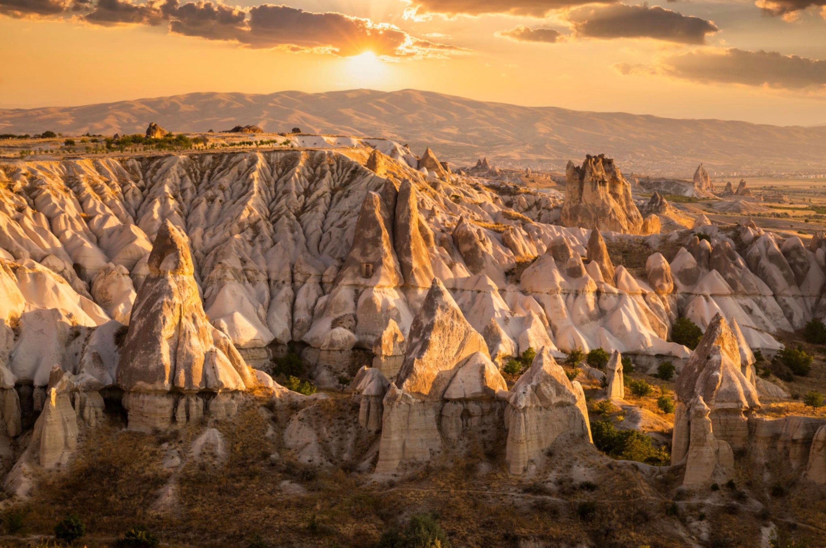 Golden sunlight illuminates unique rock formations and valleys under a cloudy sky.