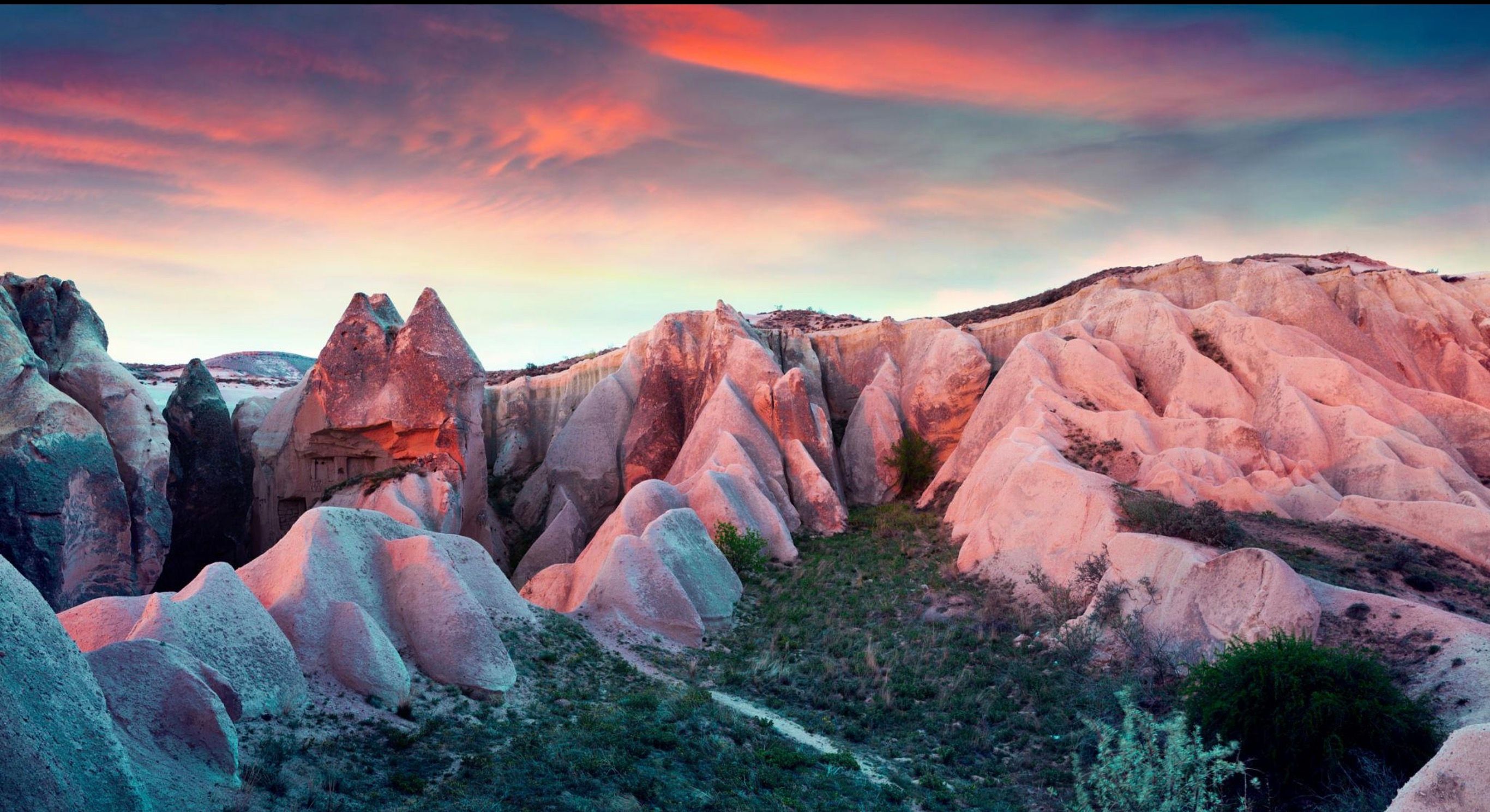 Pink volcanic rock formations in a valley under a colorful sunset sky.