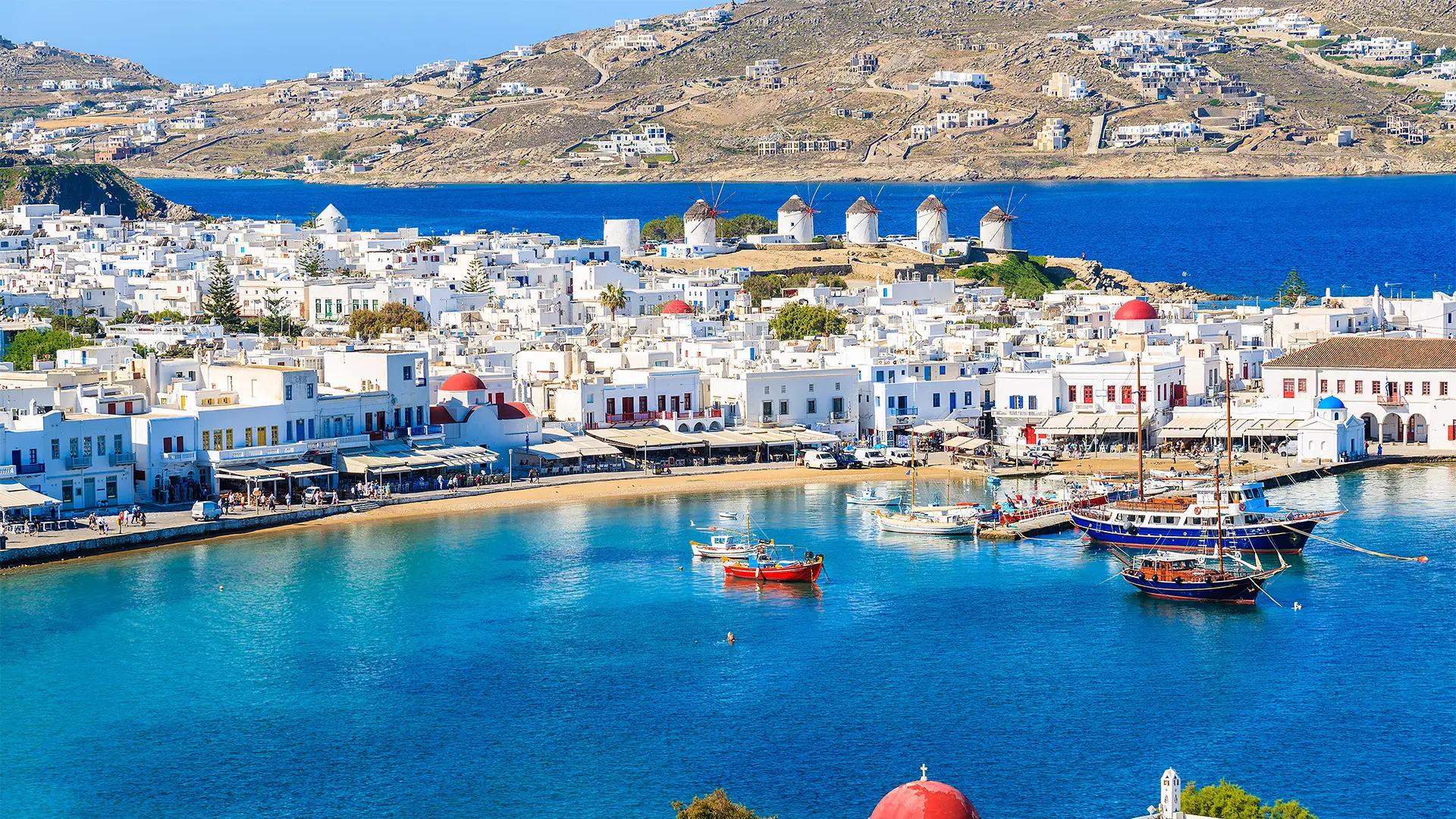 Whitewashed Mykonos town, iconic windmills, and a vibrant blue harbor filled with boats.