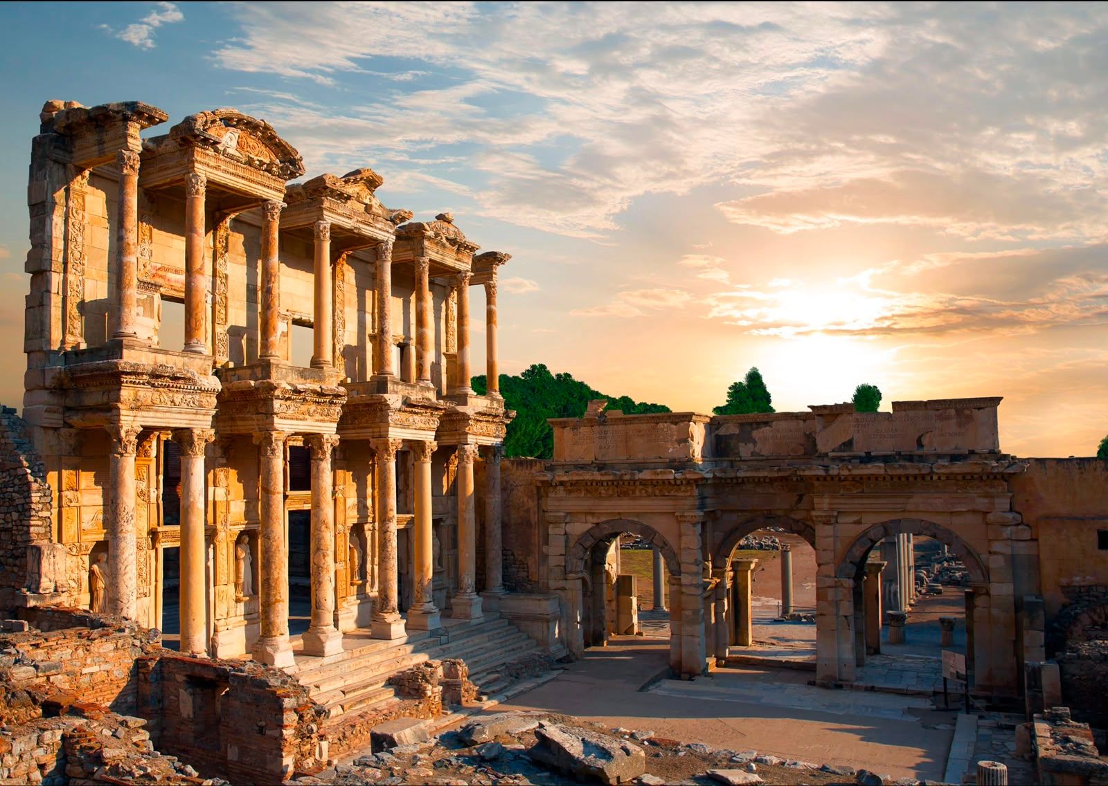 Ancient stone columns and arches of Roman ruins under a cloudy sunset sky.