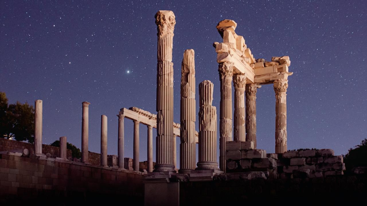 Illuminated ancient temple ruins with tall columns under a starry night sky.