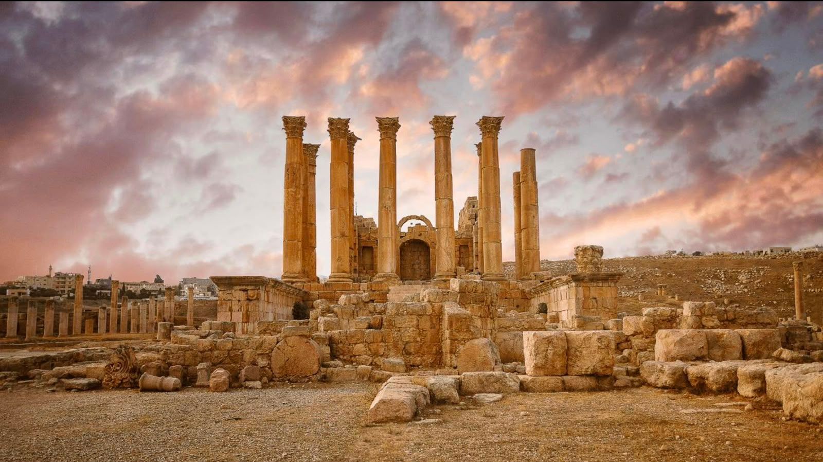 Tall ancient stone columns rise against a cloudy sunset sky.