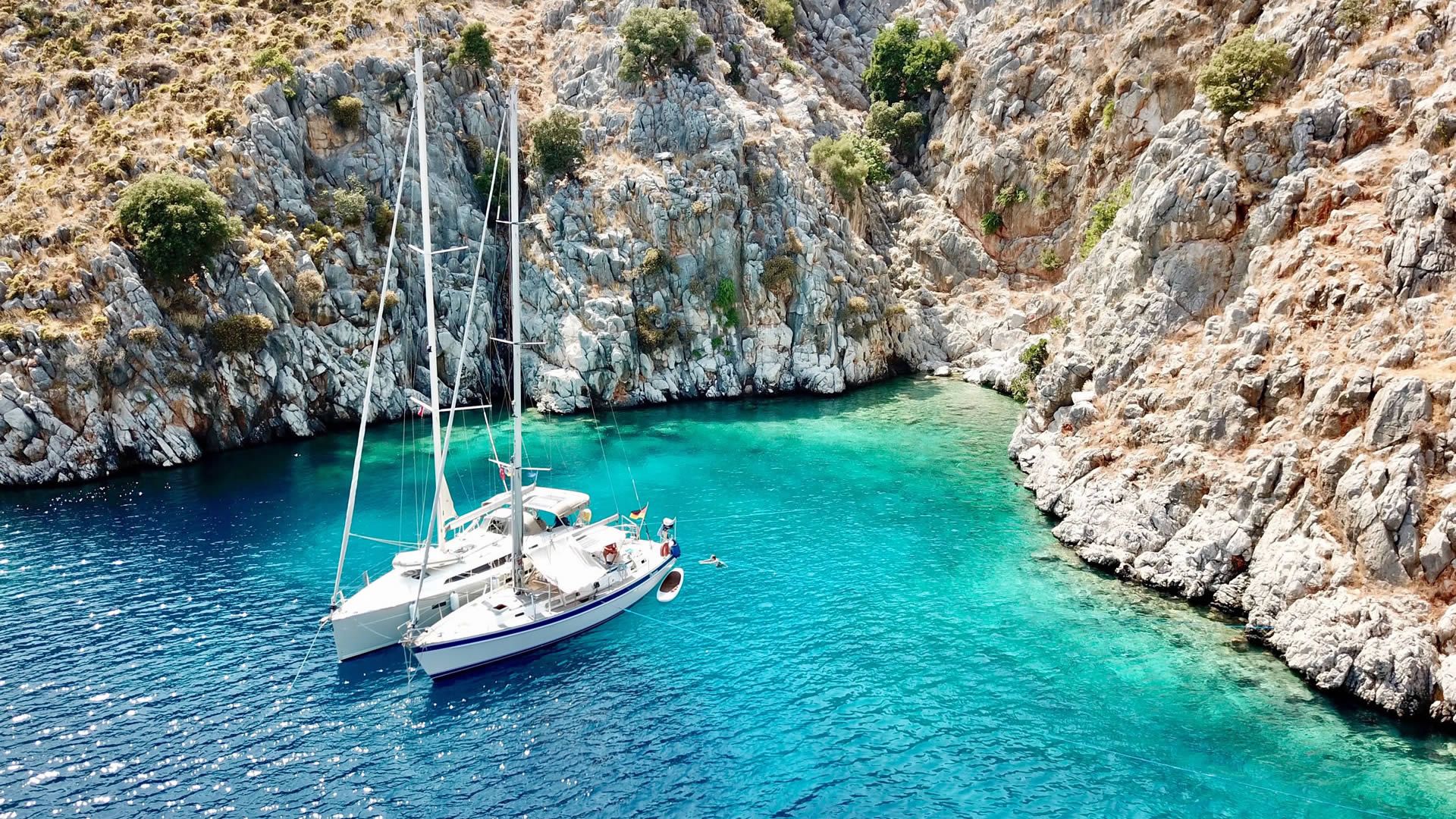 A white catamaran anchored in a clear turquoise bay surrounded by rocky cliffs.