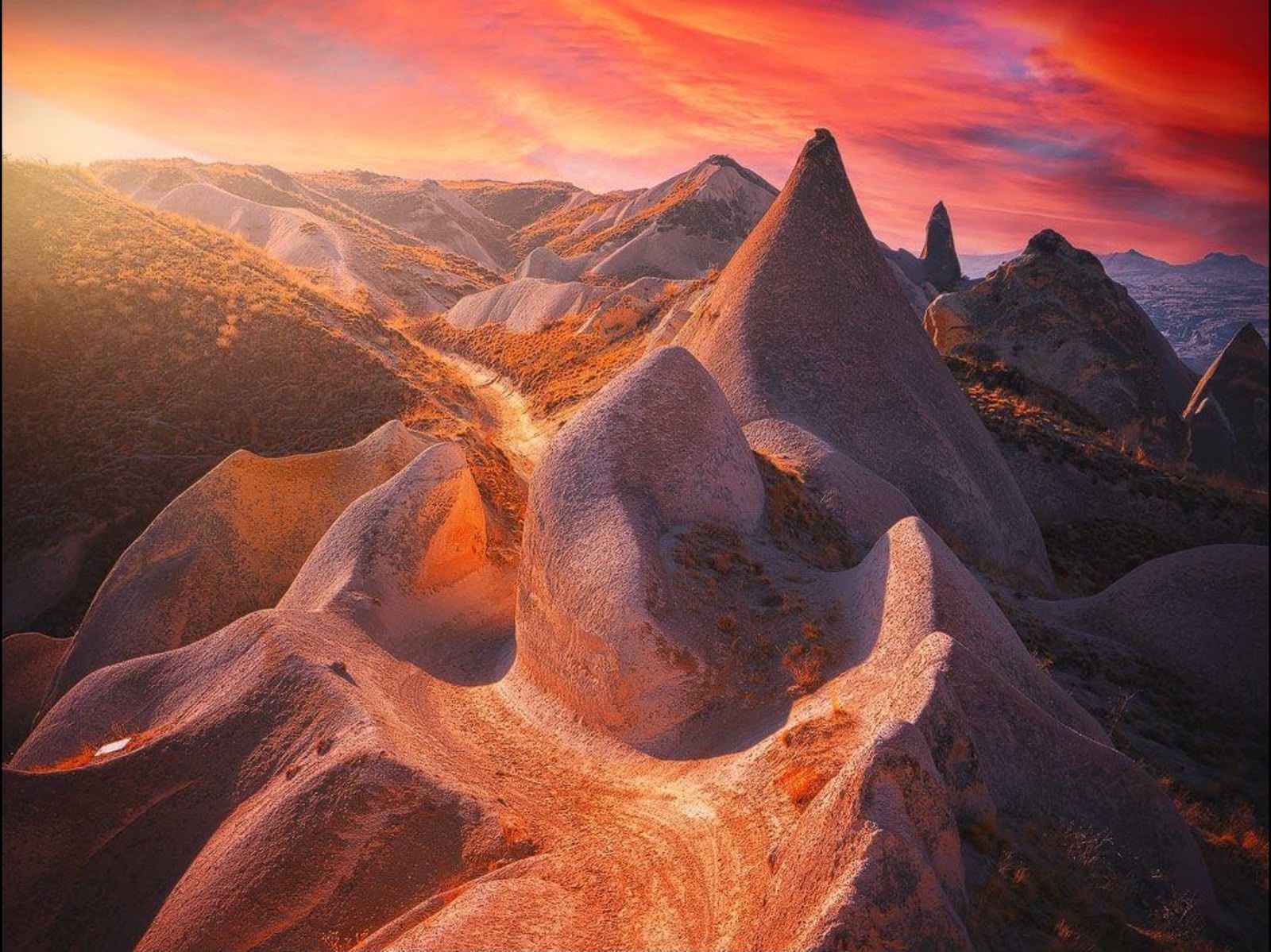 Conical volcanic rock formations under a vibrant orange and red sunset sky.