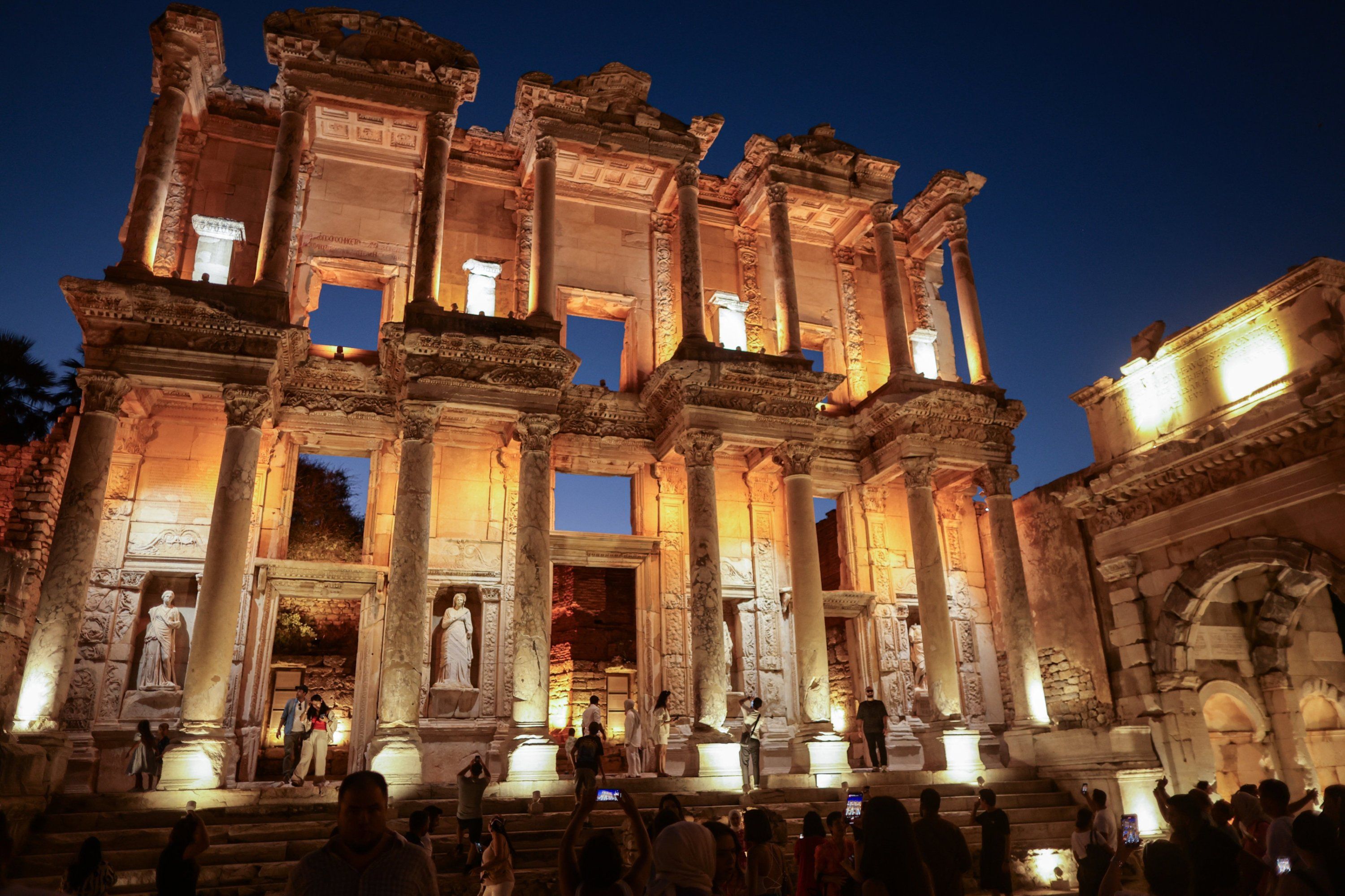 The illuminated Library of Celsus in Ephesus at night, with visitors on its grand steps.