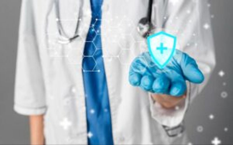 A doctor wearing a white coat, blue tie, and blue gloves holds out a hand with a digital shield and medical cross icon, symbolizing healthcare and protection. Hexagonal tech graphics overlay the image.