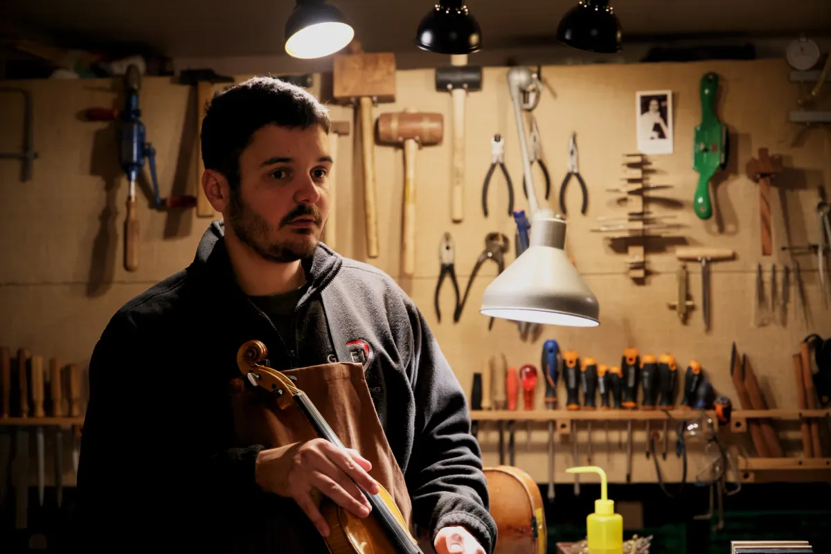 Nicolas Wicky dans son atelier, un violon à la main, devant le mur d'outils.