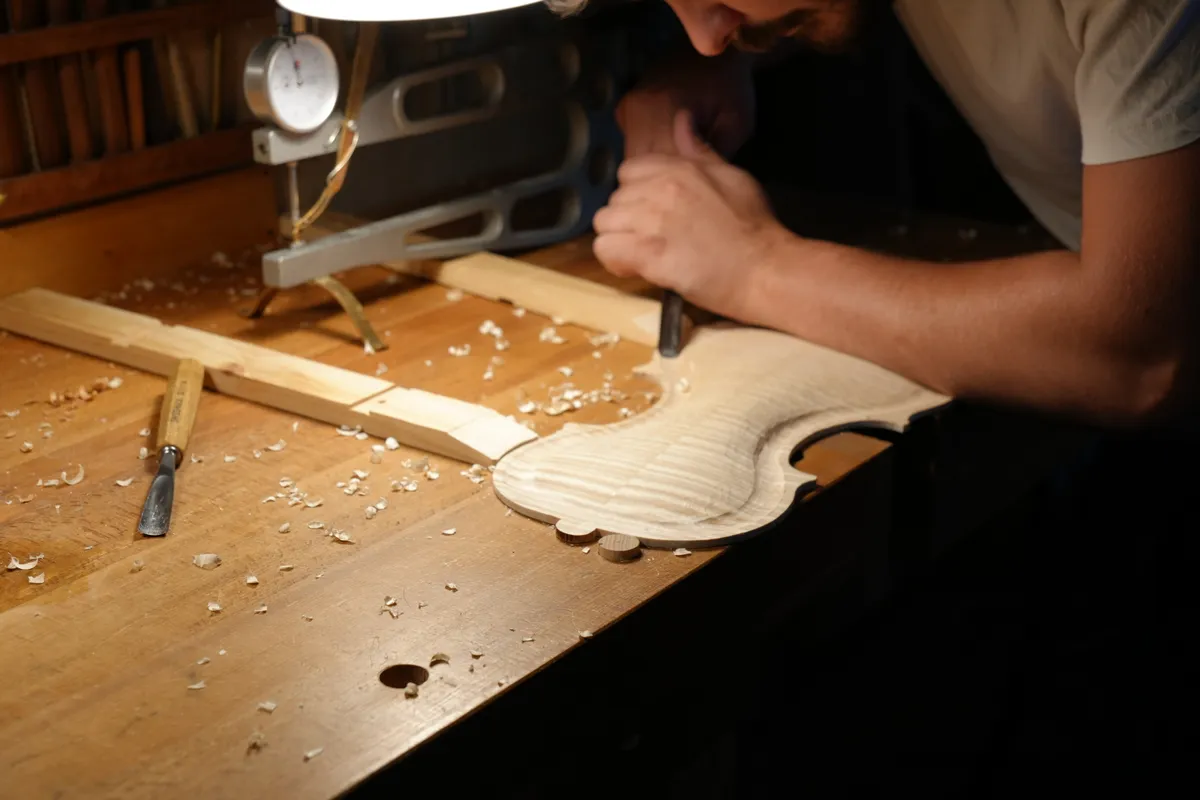 Les mains du luthier travaillent à la gouge un fond de violon en érable ondé.