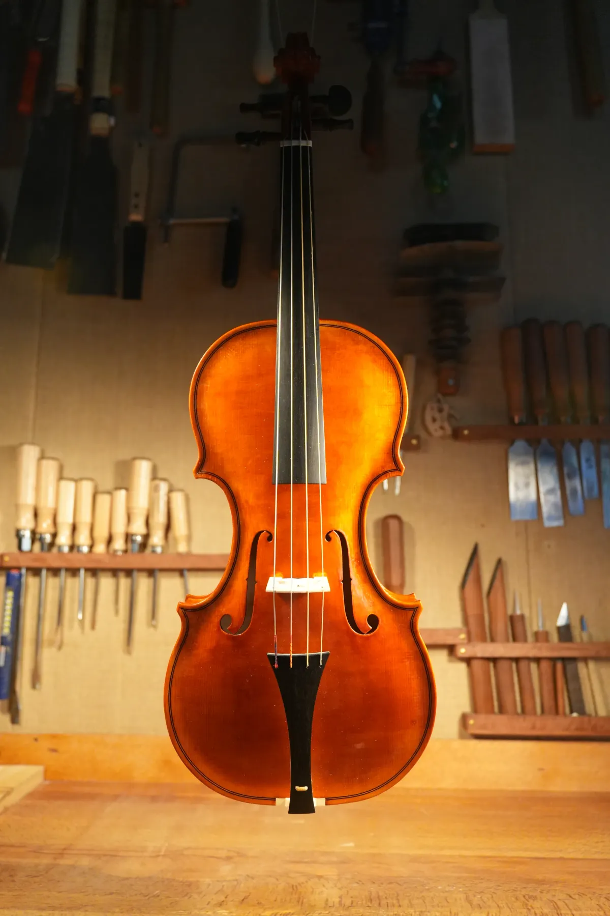 Un violon terminé, suspendu devant le mur d'outils de l'atelier.