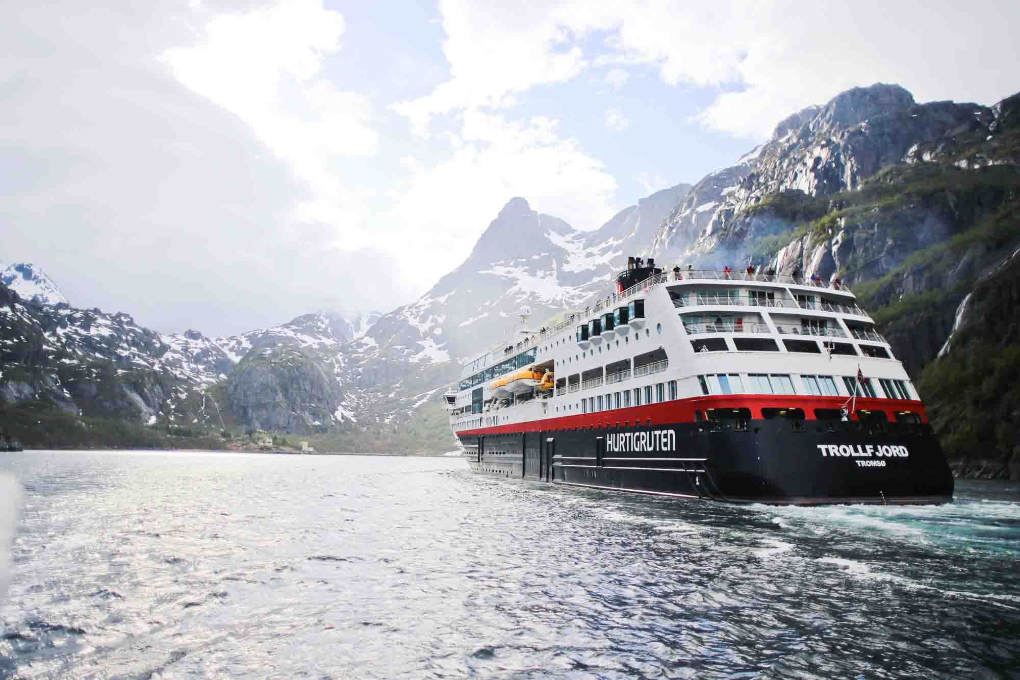 Hurtigruten Trollfjord Tromsø seiler på en fjord med høye fjell i bakgrunnen.