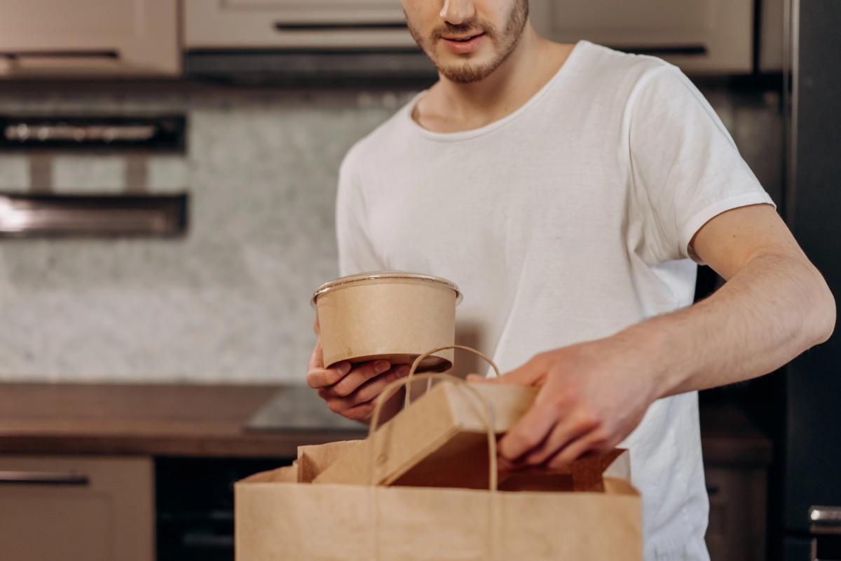 A person in a white shirt holding a takeaway bowl and a paper bag.
