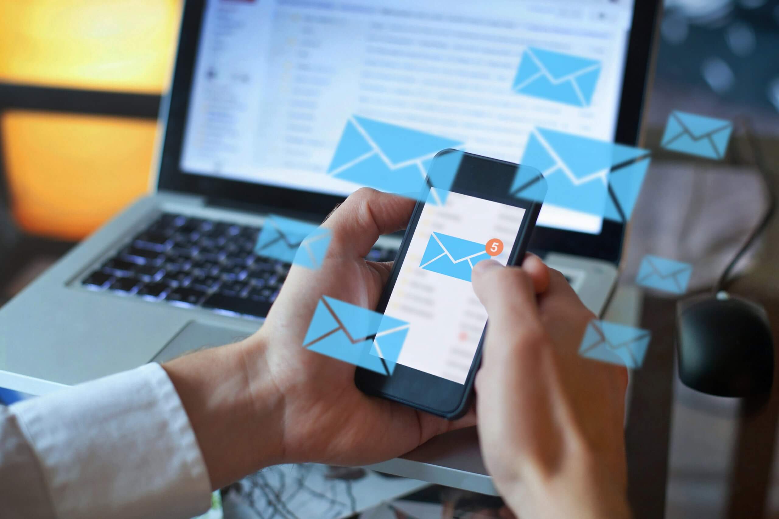 A man holding a smartphone with email icons popping up on the screen.