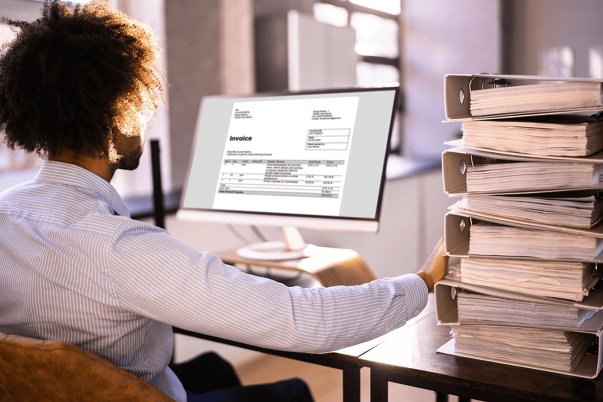 A man sitting in front of a computer screen, reviewing invoice.