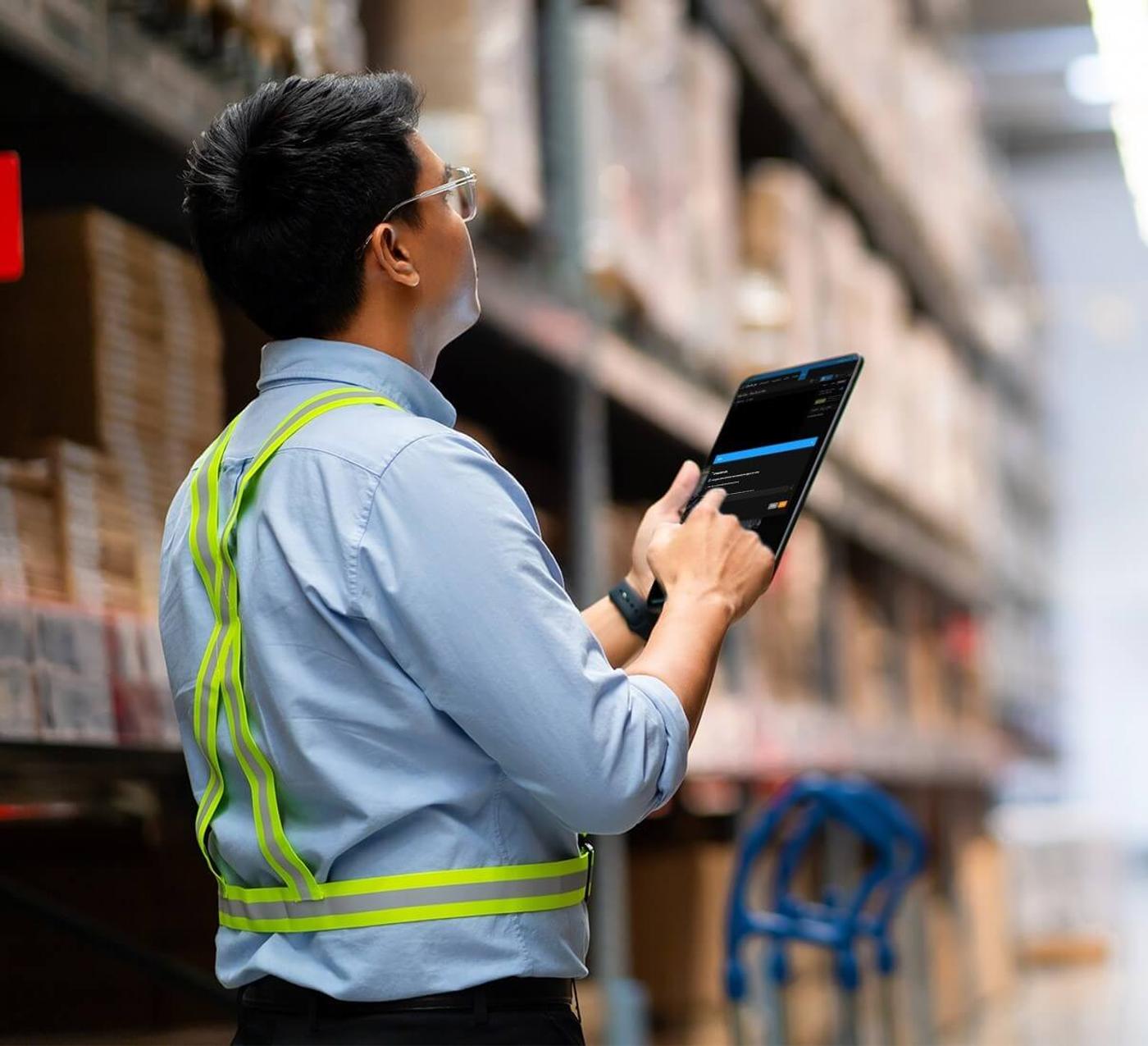 A man conducting inventory in a warehouse while holding a tablet to record stock data.