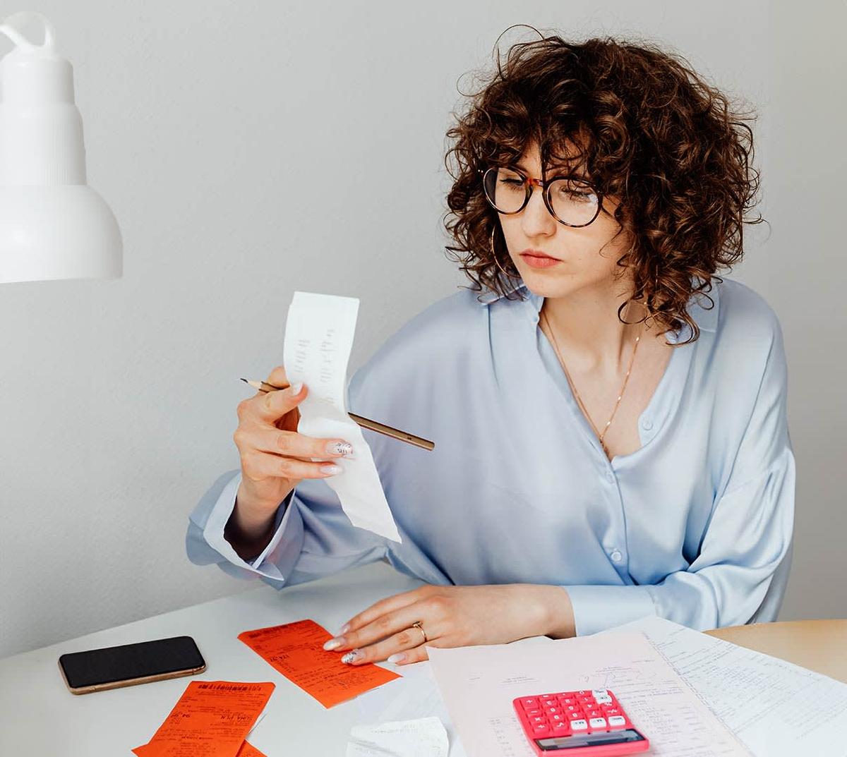 A woman with curly hair sitting at a desk, busy with receipt and a pen in hand.
