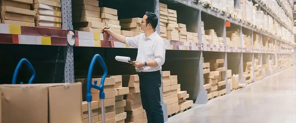 Worker checking warehouse shelves with a paper pick list.